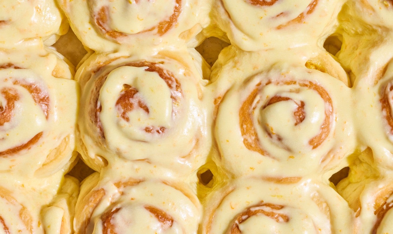 Detail shot of several Fluffy Frosted Orange Rolls together seen from above with a glossy yellow citrus glaze.