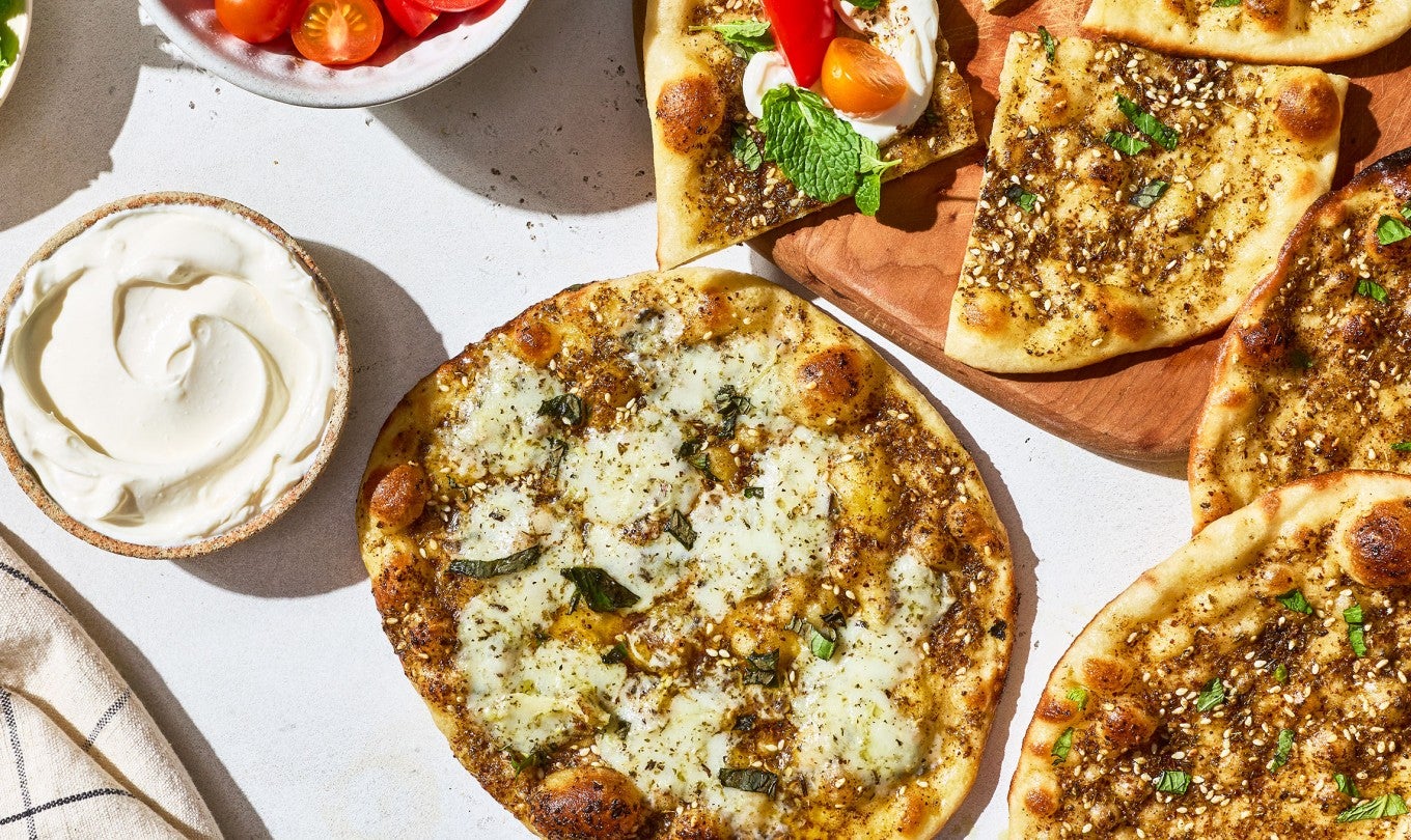 Za’atar Manakeesh spread out with toppings, dip, herbs, and veggies.
