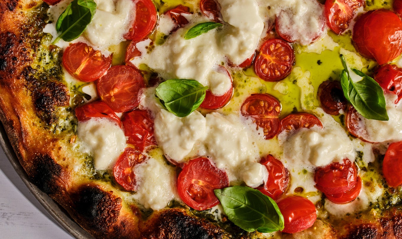 A detailed shot of caprese style New York pizza showing mozzarella, basil, and tomatoes.