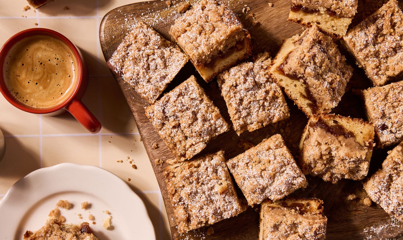 Apple Crumb Cake sliced up and arranged on a cutting board with a cup of coffee in the frame