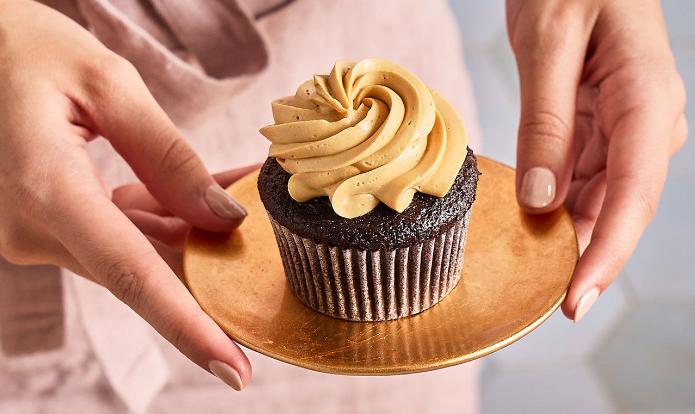 Holding a plate with a Chocolate Cupcake with Whipped Caramel Frosting on it