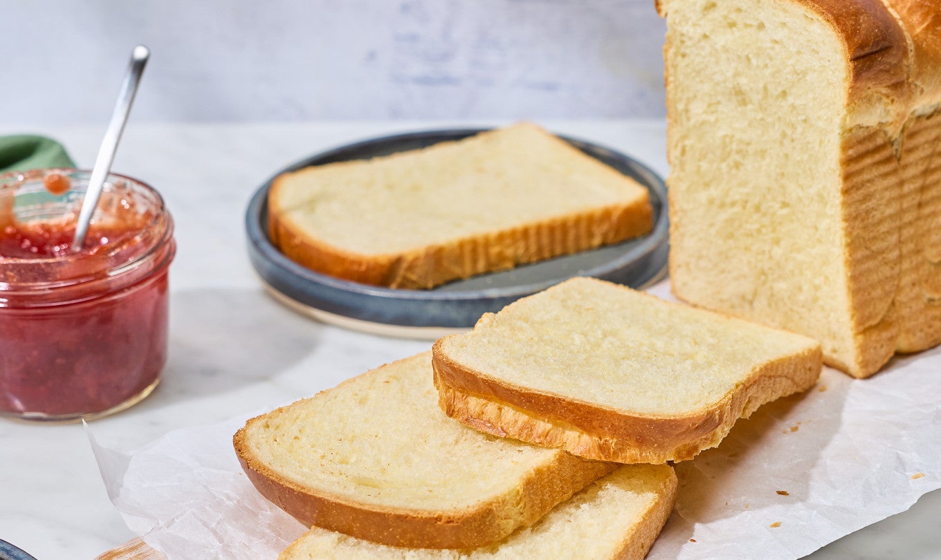 Sourdough Milk Bread sliced on a counter with a jar of preserves