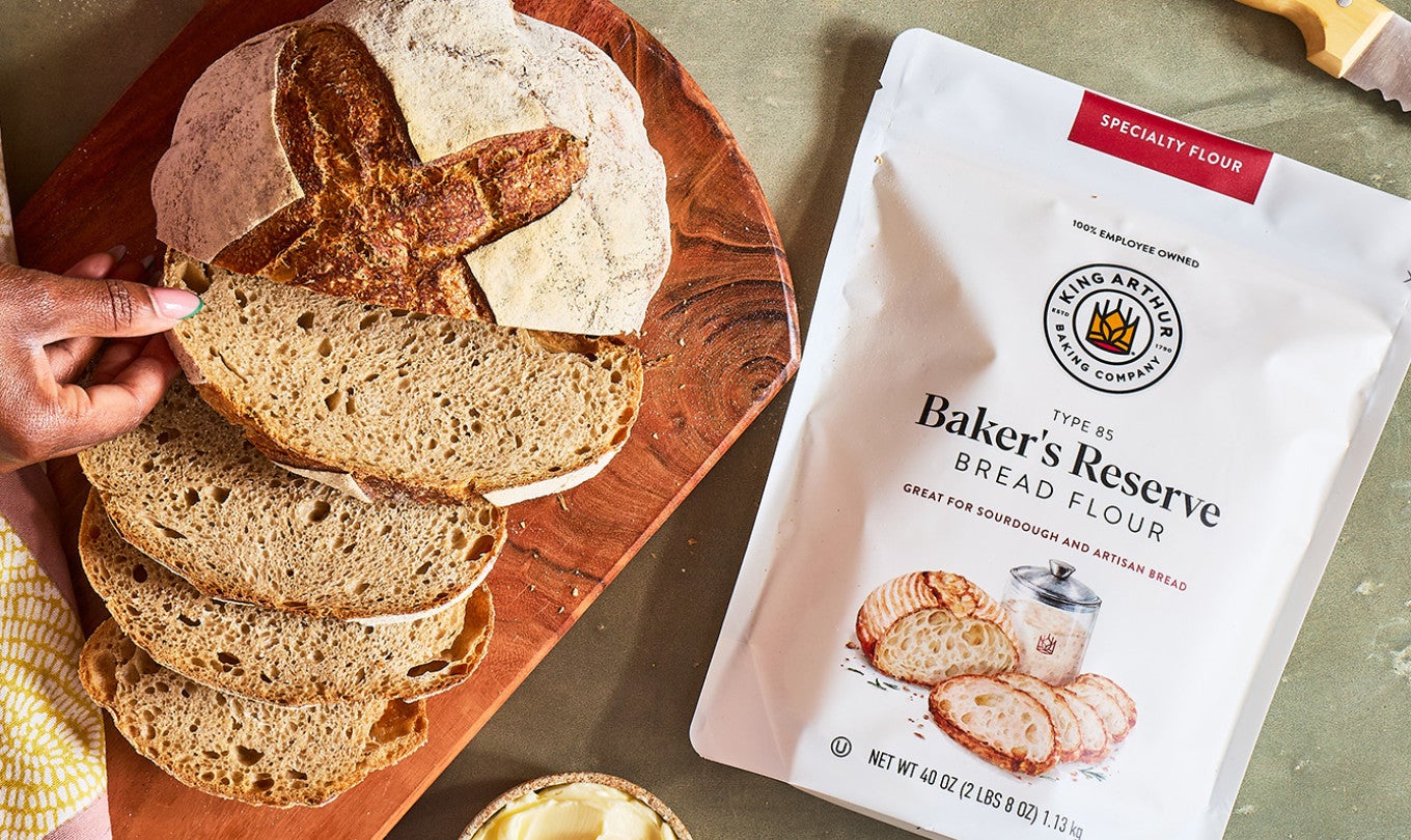 A bag of King Arthur Baking Baker's Reserve Bread Flour and a loaf of sourdough bread