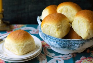 Golden soft dinner rolls in a bowl, one on a bread plate.