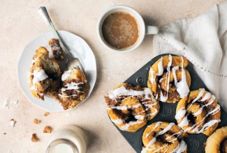 A tray of gluten-free cinnamon rolls next to a cup of coffee and plate with a cinnamon roll on it