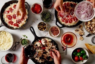 Three cast iron pan pizzas being topped with different ingredients