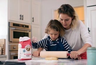 A mother and son using a rolling pin to roll out cookie dough