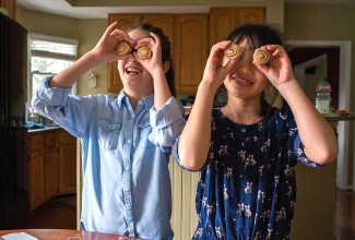 Two older kids being silly by holding cinnamon rolls up as if they were eyes