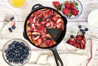 A sweet pizza topped with strawberries and chocolate on a table set for brunch