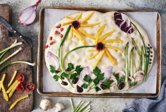 Focaccia dough topped with vegetables arranged in a garden scene
