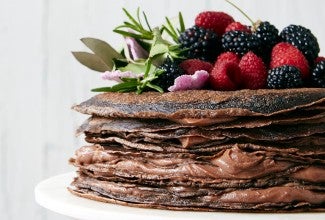 A chocolate cake made from stacked crepes and filled with pastry cream, topped with berries