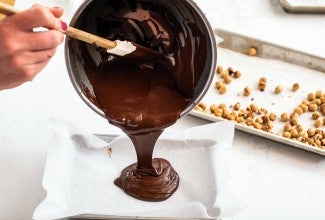 A baker pouring melted chocolate onto a sheet pan to make chocolate bark