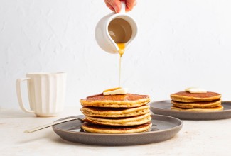 Syrup being poured onto a stack of pancakes