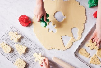 Hands cutting out sugar cookie dough in festive shapes