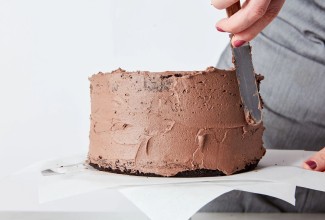 Chocolate layer cake being crumb coated with chocolate frosting