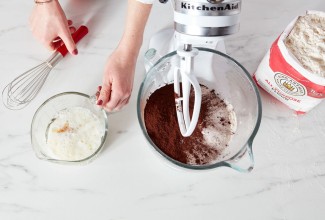 Ingredients for chocolate cake being added to a stand mixer bowl