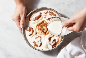 Heavy cream being poured over a pan of risen cinnamon rolls prior to baking.