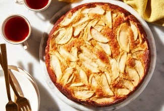 A freshly baked Mostly Apples Apple Cake next to two cups of tea and forks