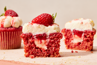 Bright red cupcakes cut in half with cream cheese and strawberry filling showing.