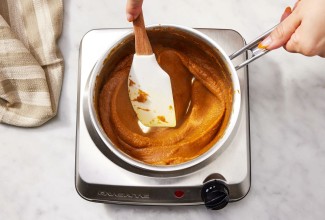 A baker cooking down pumpkin puree in a saucepan on the stovetop