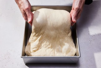 A baker folding wet dough in a square pan with their hands