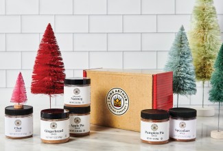Holiday spice gift kit in front of small decorative Christmas trees