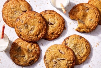 A few big chocolate chip cookies on a kitchen counter with glasses of milk