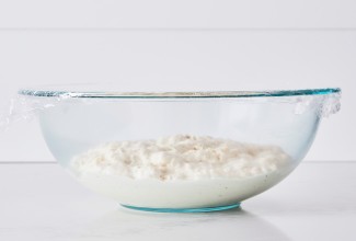 Bread dough in clear glass bowl with plastic wrap covering