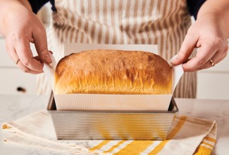 Baker lifting loaf of bread out of pan with silicone pan liner