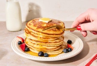 Easy Buttermilk Pancakes topped with maple syrup on a plate with fresh fruit