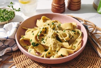 Cooked gluten-free pasta in a pink bowl with herbs and cheese.