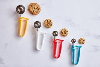 Different sizes of kitchen scoops next to chocolate chip cookies