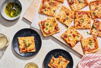 Slices of Gluten-Free Sheet Pan Pizza seen from above and randomly arranged on a cutting board with other slices on plates.