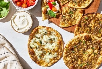 Za’atar Manakeesh spread out with toppings, dip, herbs, and veggies.