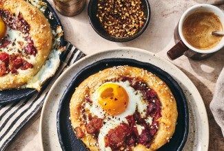 Breakfast Shakshuka shown on a plate with coffee and hot pepper flakes also in the picture.