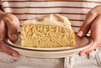 A slice of Frosted Brown Butter Cake being held on a plate seen from the side