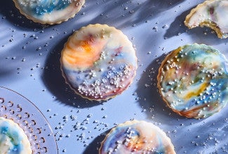 Northern Lights Iced Sugar Cookies arranged on a blue background surrounded by sprinkles of sparkling sugar