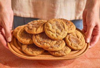 Pumpkin Snickerdoodle Cookies stacked and arranged on a plate with someone holding the plate up