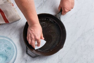 cast iron pan being cleaned with a sponge