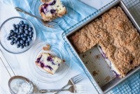 A pan of Blueberry Buckle Coffeecake with a few slices next to it on plates, along with fresh blueberries