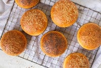 Homemade hamburger buns topped with seeds cooling on a rack