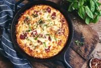 A Gluten-Free Pan Pizza in a cast iron pan on a wooden table garnished with fresh herbs