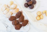 A platter of chocolate and vanilla madeleines shaped traditionally next to a few madelelines shaped like mini muffins