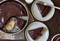 A chocolate cake pan cake topped with chocolate frosting and a few slices on plates