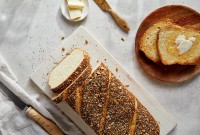A loaf of chewy semolina rye bread cut into slices with a few pieces toasted on a plate