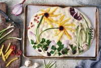 Focaccia dough topped with vegetables arranged in a garden scene