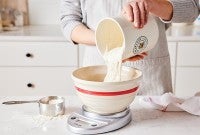 A baker pouring sourdough starter into a bowl to prep it for baking