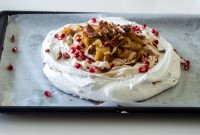 Winter pavlova topped with pomegranate seeds, baked apples, and nuts
