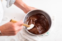 Baker stirring bowl of melted chocolate with a spatula 