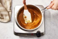 A baker cooking down pumpkin puree in a saucepan on the stovetop